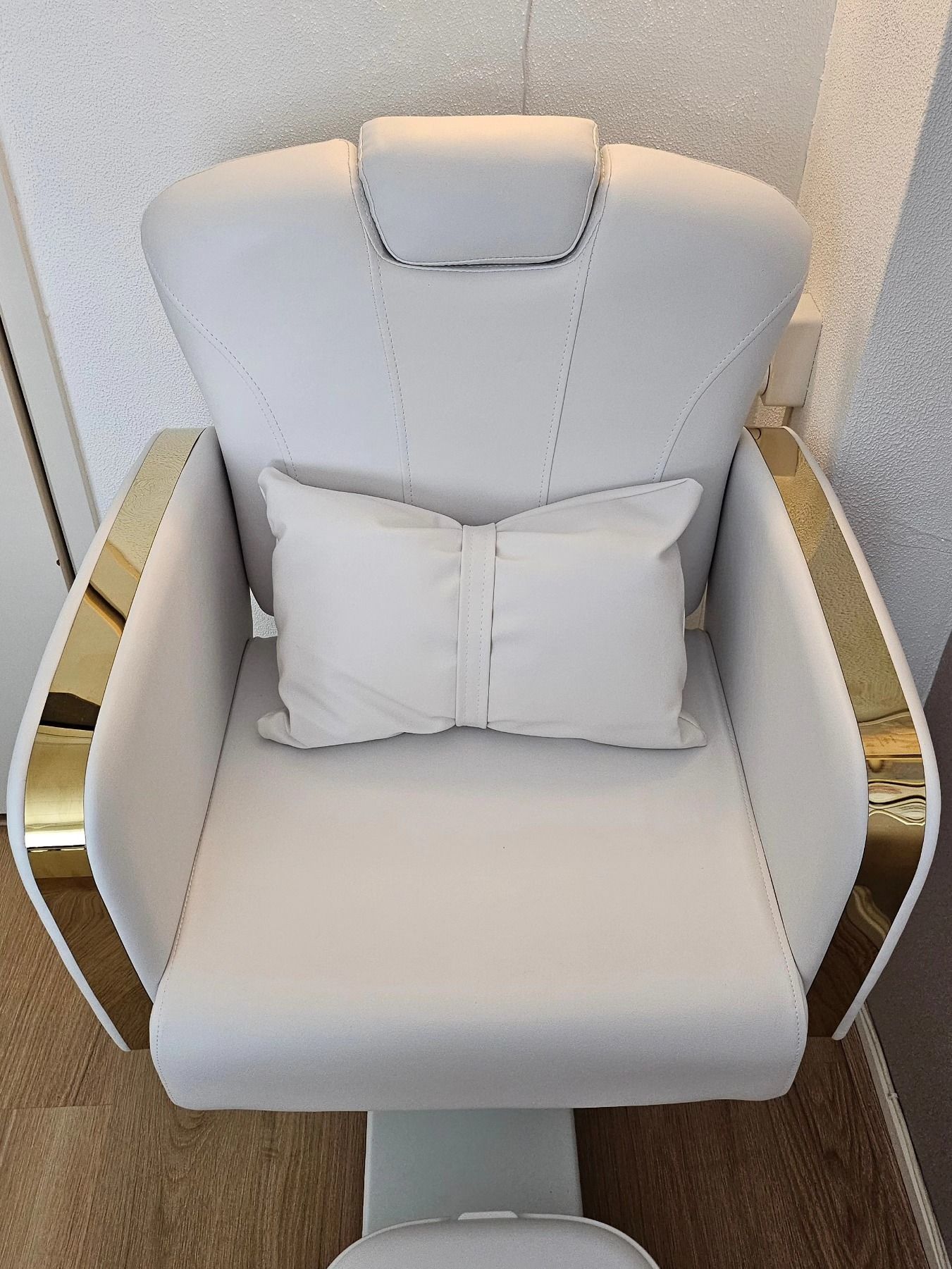 De pedicurestoel in de salon, wit leer met gouden zijkanten en een kussen met strik