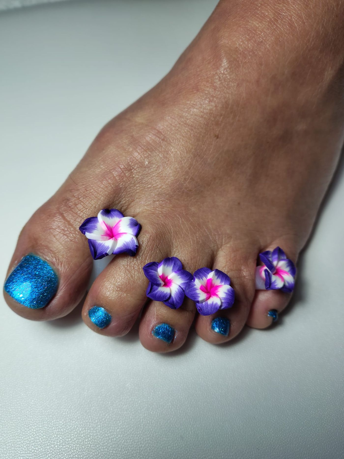 Blauwe glittergellak op de teennagels met bloemen als teenspreiders