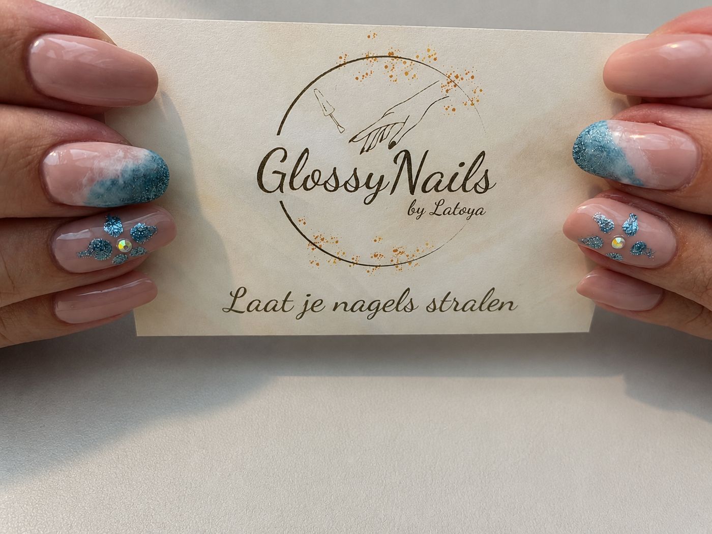 Een klant houdt het visitekaartje van Glossy Nails by Latoya vast, haar nagels in blauw en wit