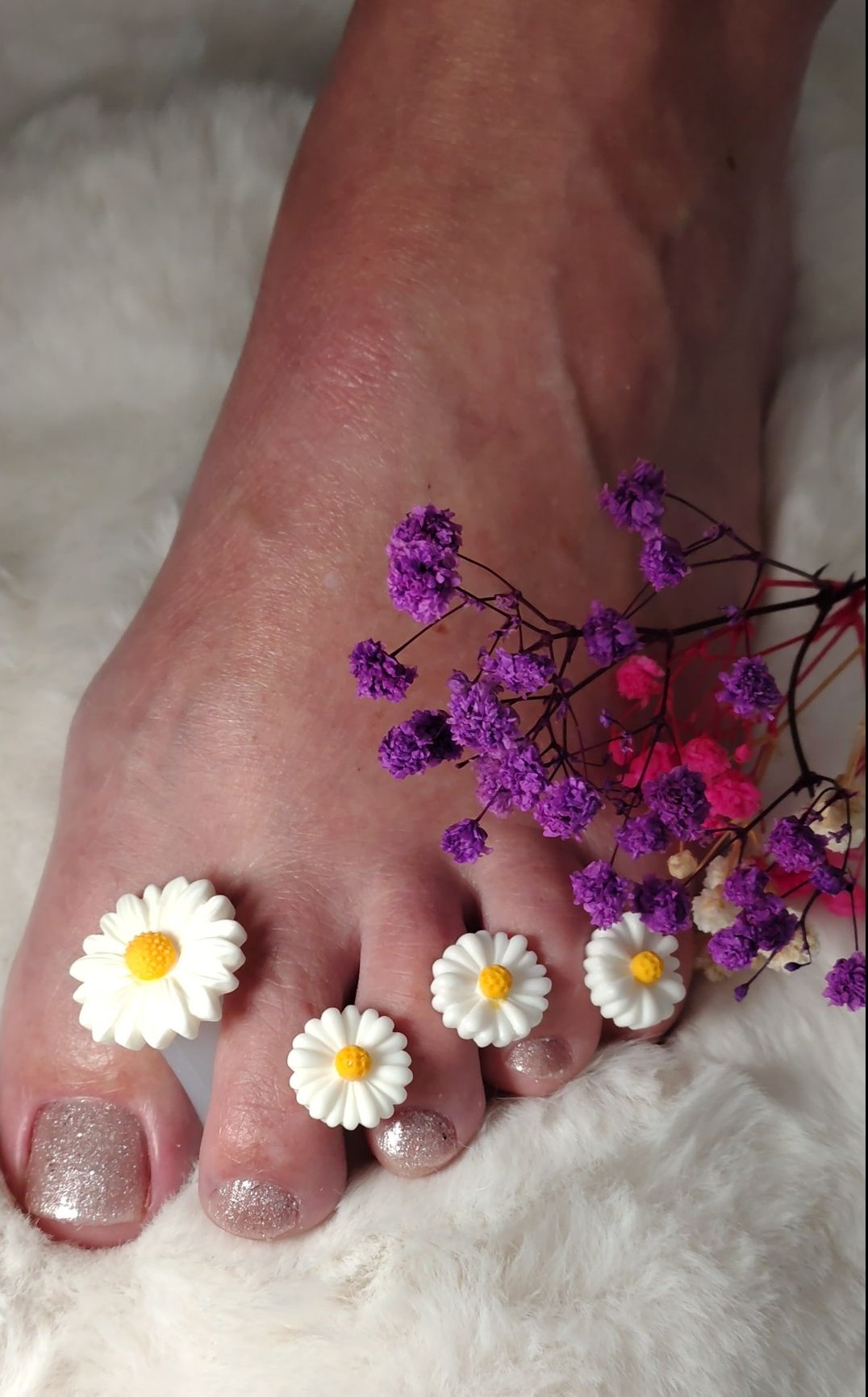 Voet met madeliefjes tussen de tenen en gedroogde bloemen